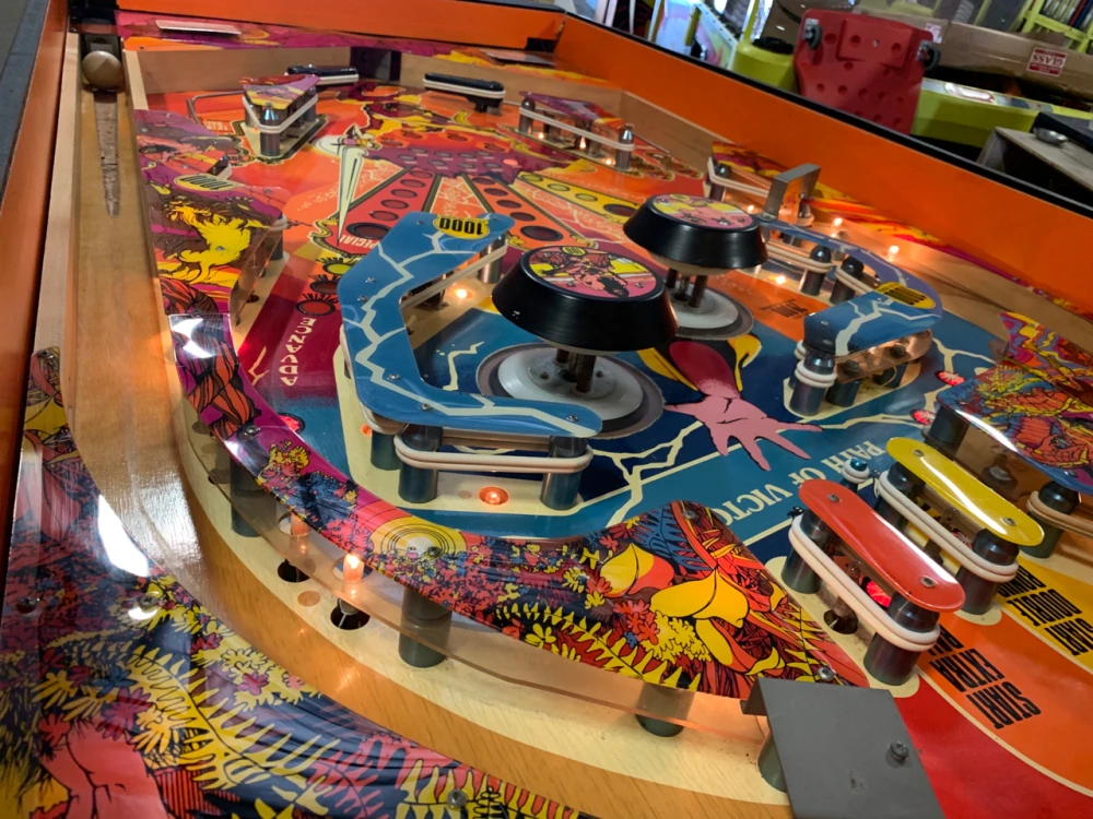 Pinball playfield close-up (example feature image) Close-up of a vintage pinball playfield with orange, purple and yellow artwork, large black mushroom bumpers, and a ball in the shooter lane